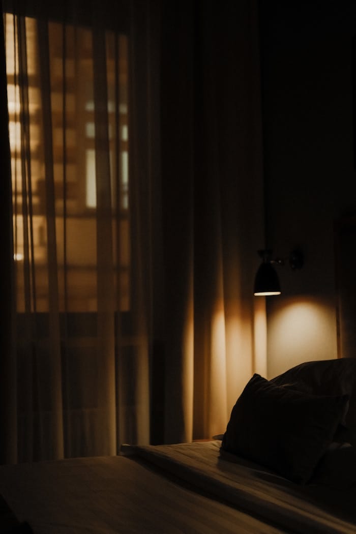 Dark, ambient hotel room with bed and soft lighting through curtains.